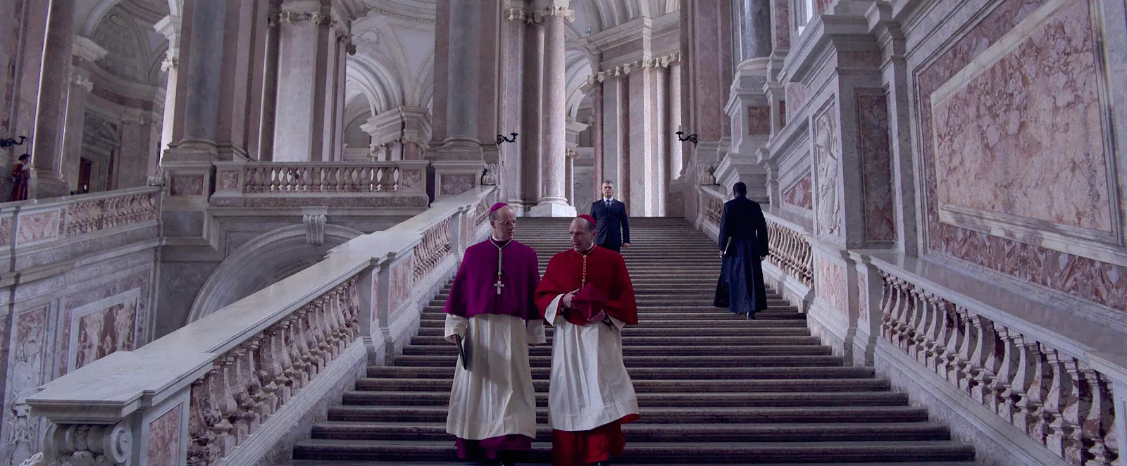 Ralph Fiennes and Brían F. O'Byrne in clerical dress in a long institutional corridor